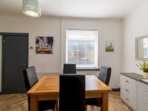 A dining area with a wooden table and four chairs, a window with blinds, a door, and a wall-mounted light fixture.