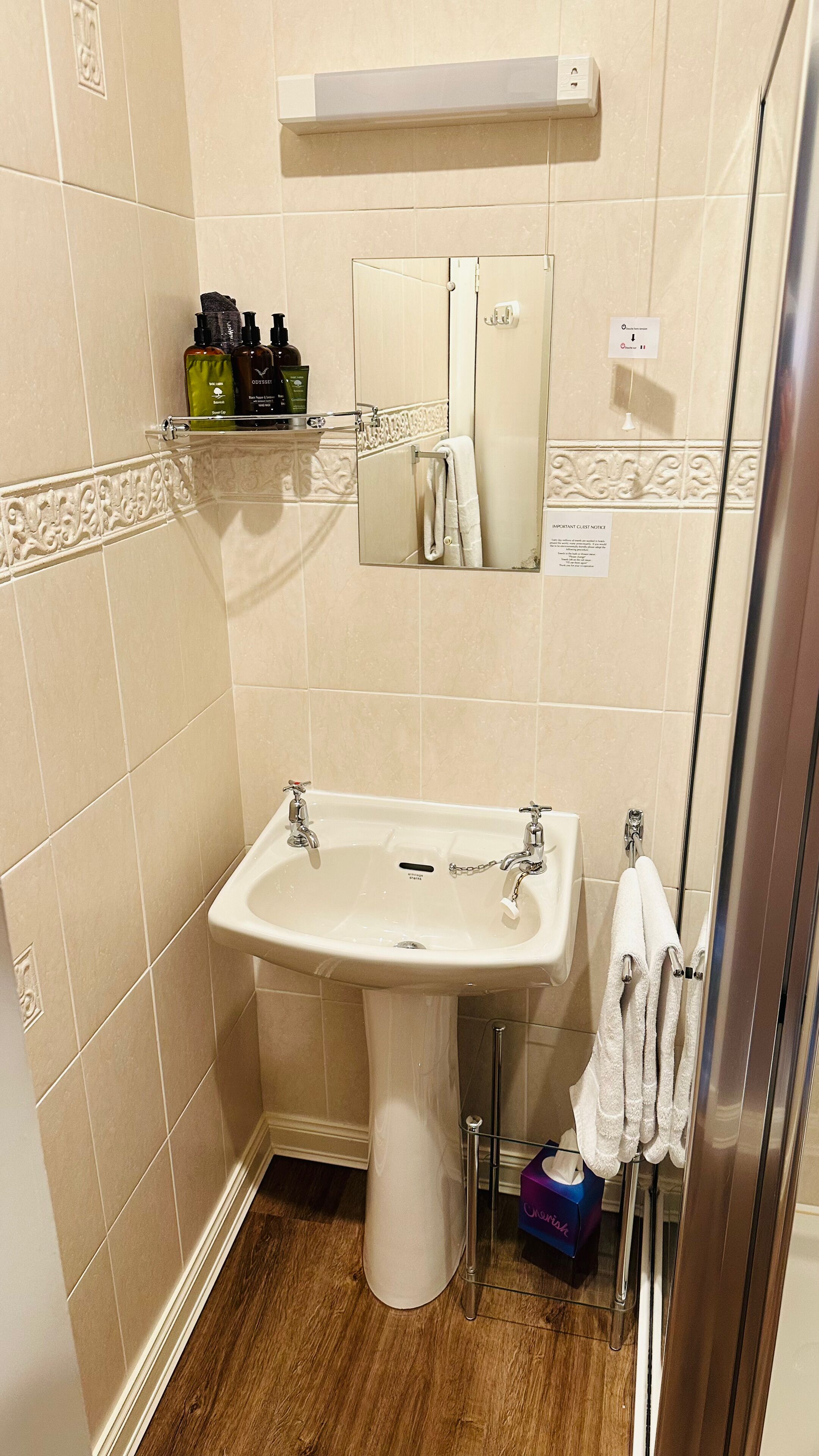 A bathroom with a pedestal sink, a mirror, a towel rack, and toiletries on a shelf.