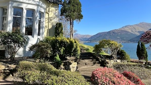 A house with a bay window, a stone staircase, and a view of mountains and a lake. - Camus House (Onich)