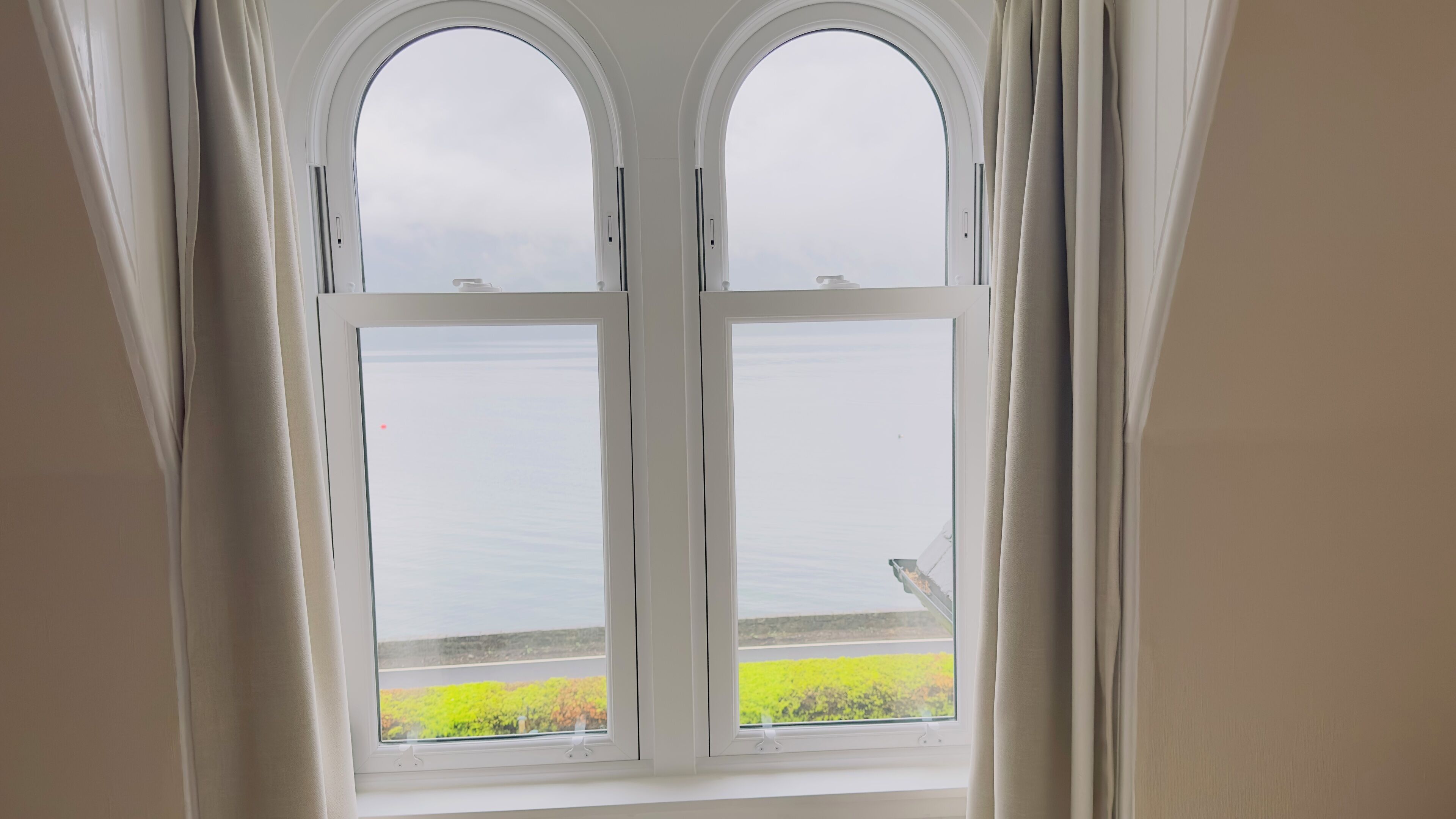 A room with a large arched window overlooking a body of water and a green landscape.