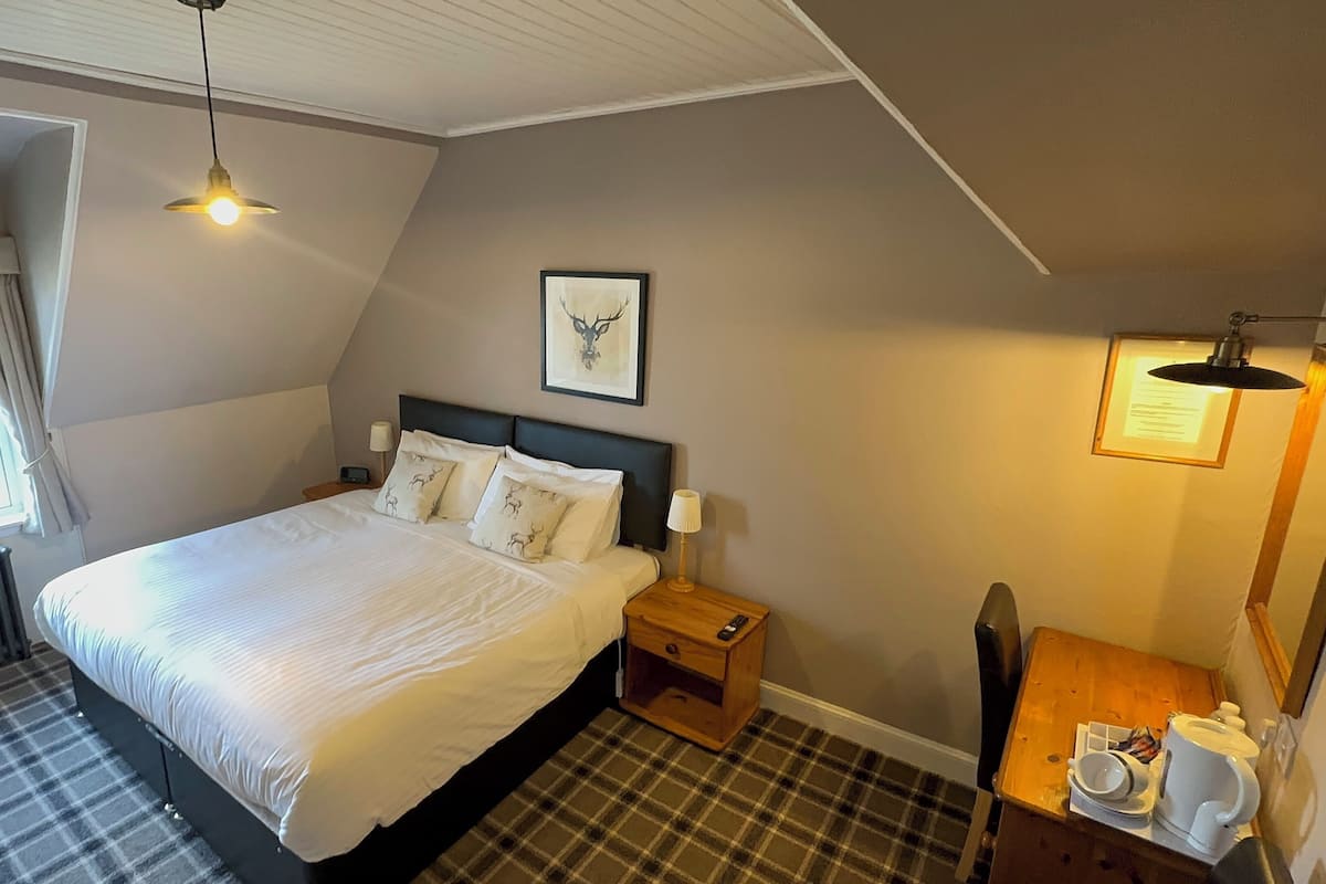 A bedroom with a bed, a nightstand, a bedside table, a window, a radiator, and a wall-mounted picture.