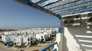 A balcony with a view of a residential area, a fan, and a small table.