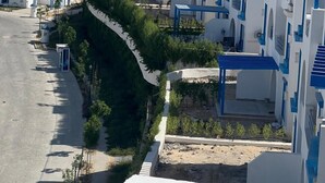 A coastal residential area with modern white and blue buildings, a paved road, and a clear view of the sea.
