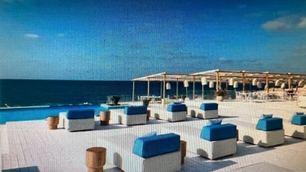 A beachside hotel with outdoor seating and a view of the ocean.