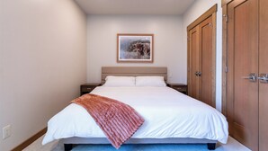 Una cama bien hecha con un edredón blanco y una manta marrón, un cuadro enmarcado de un toro en la pared y armarios de madera.