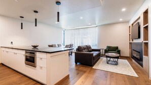 Una cocina moderna con una isla central, un área de comedor con sofá y sillones, una chimenea y un televisor montado en la pared.