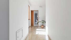 Un pasillo con una planta en maceta, una puerta que da a una habitación y una pared blanca.