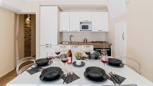 A dining area with a white table set for six, surrounded by white cabinets and a microwave above. - Casa Margot by BarbarHouse (Campomarino)