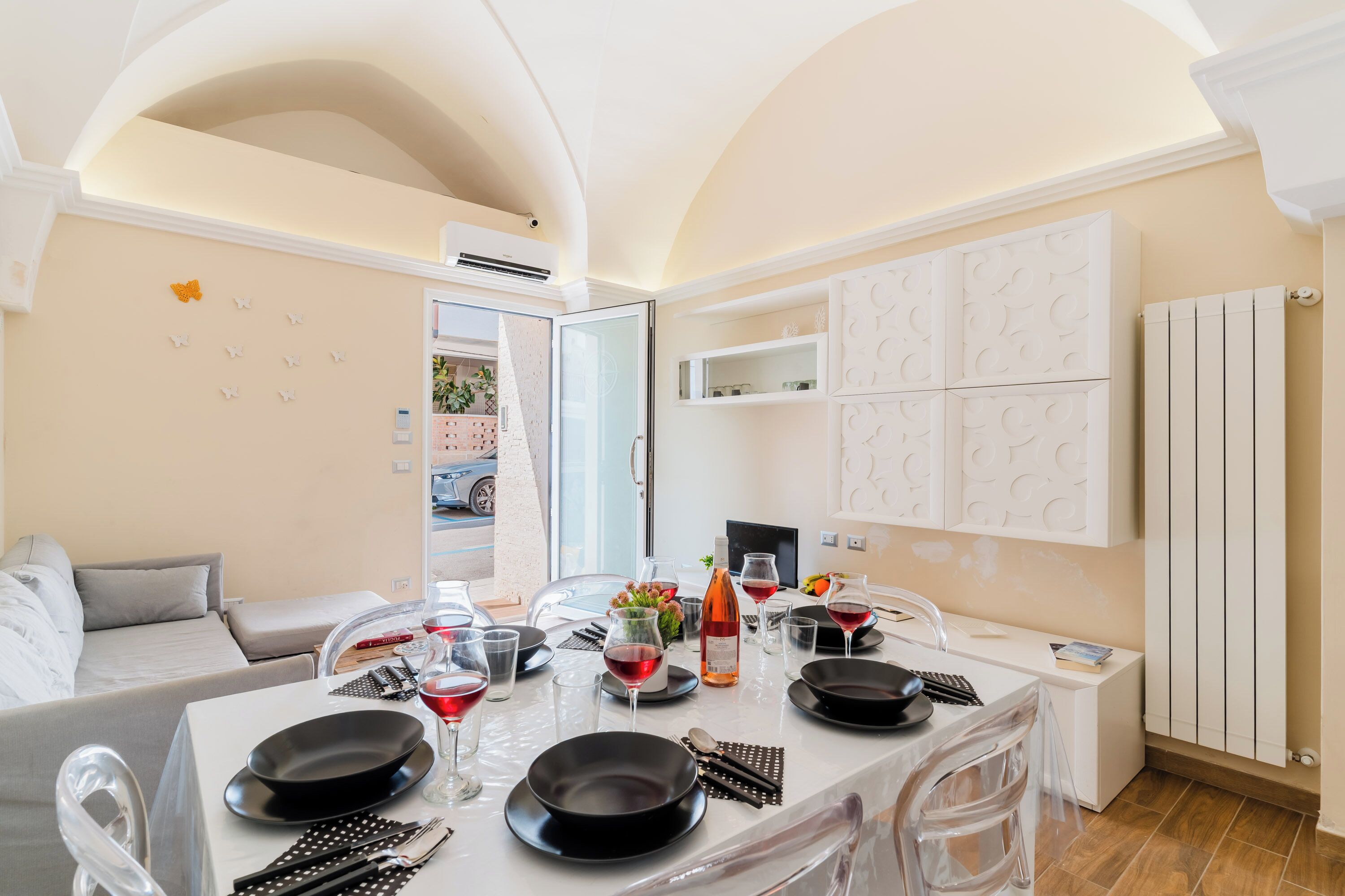 A modern dining area with a white table set for four, clear chairs, and a white cabinet with decorative panels.