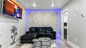 Un salon moderne avec un canapé d’angle, deux petites tables rondes et un téléviseur fixé au mur qui diffuse des services de streaming.