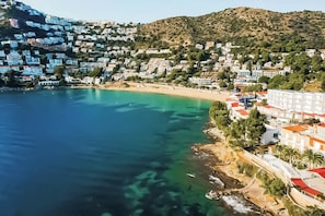 A coastal town with buildings along the shoreline, a beach, and a hilly backdrop.