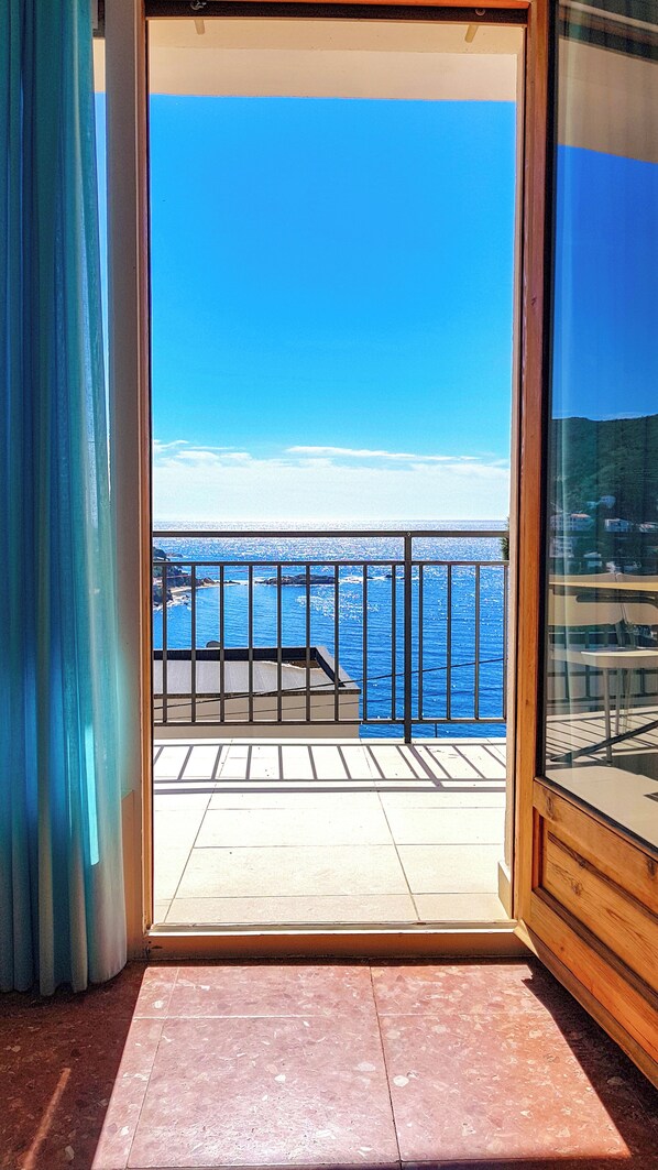A balcony with a view of the sea, a tiled floor, and a wooden door frame.