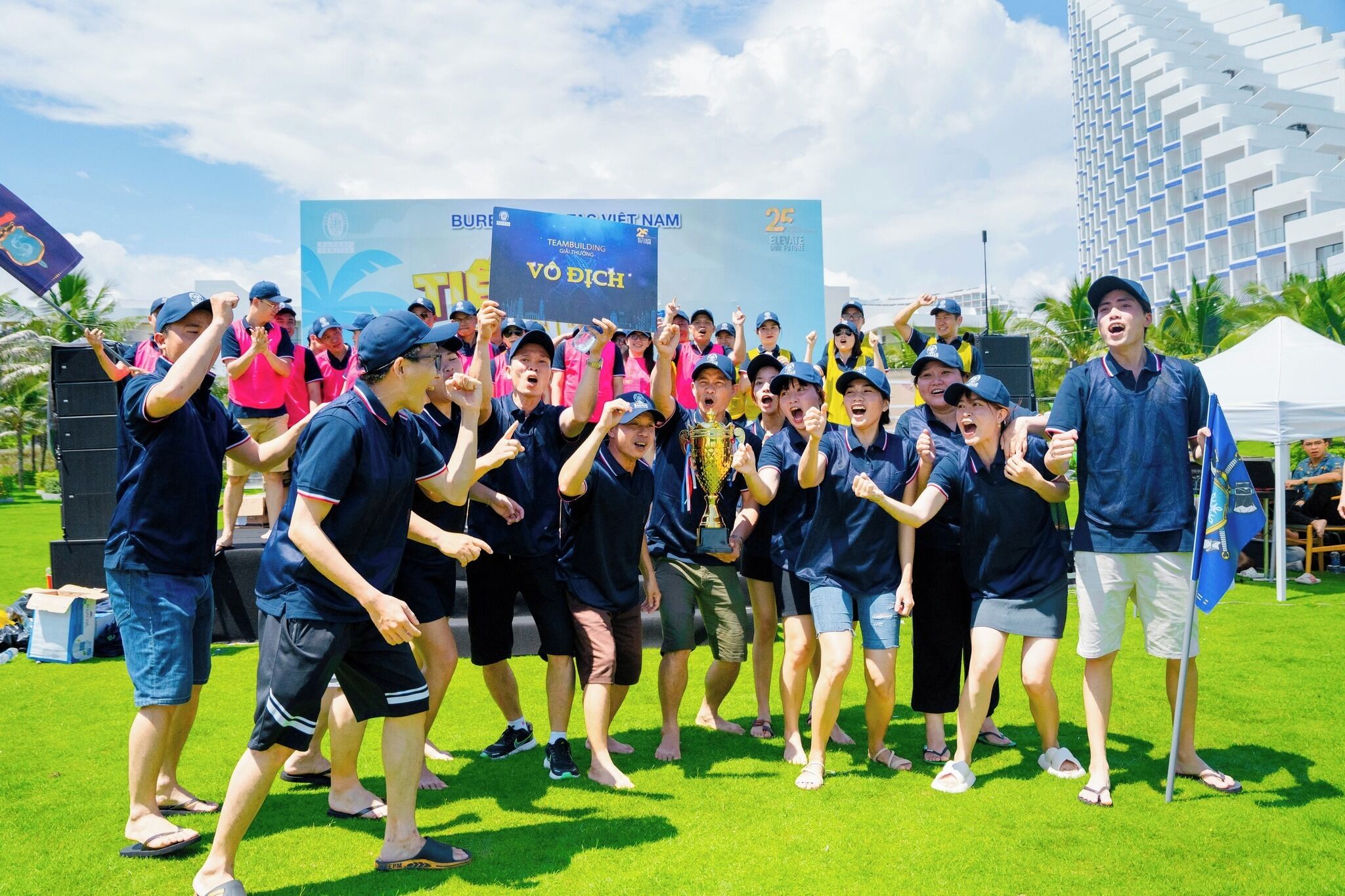 A group of people in a grassy outdoor area with a large banner in the background.
