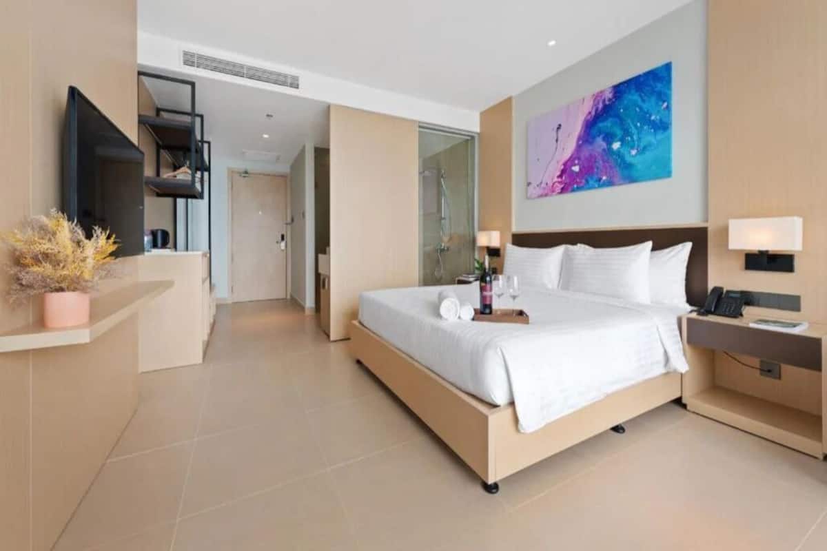 A modern hotel room with a large bed, a desk, a flat-screen TV, and a painting on the wall.