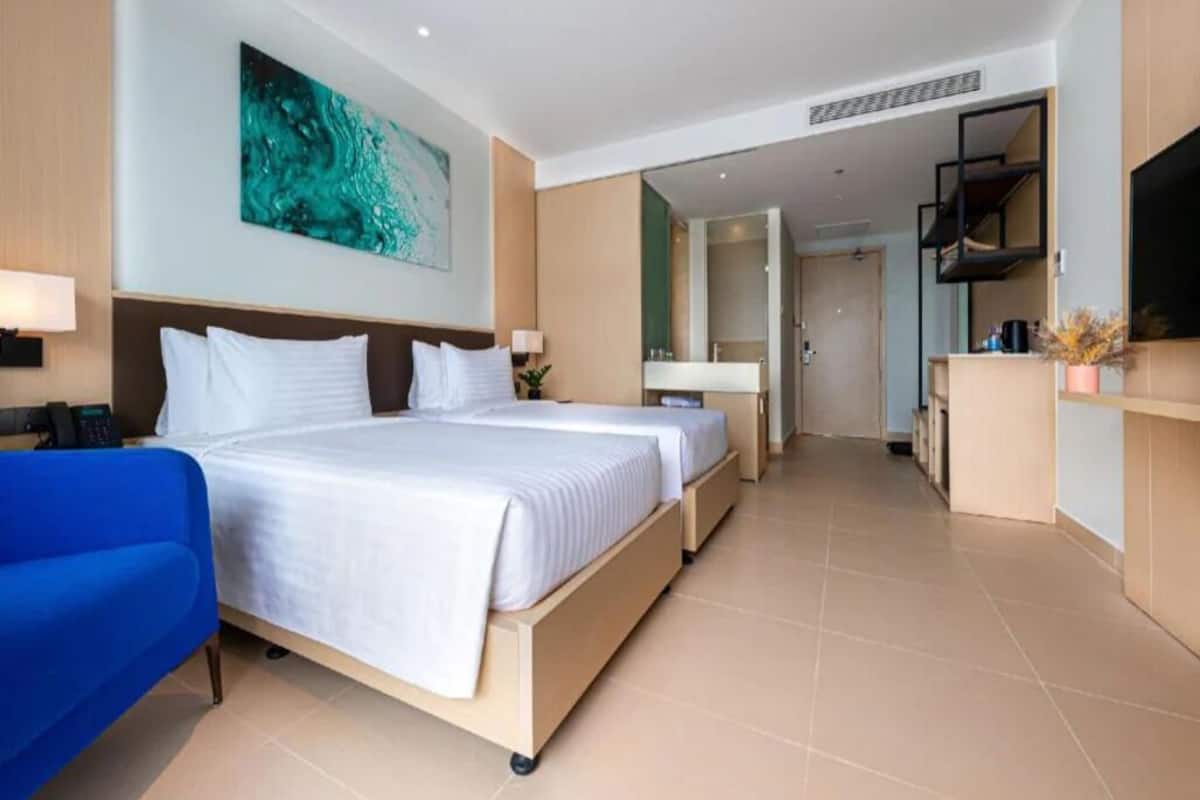 A hotel room with a large bed, a blue armchair, a TV, and a painting on the wall.