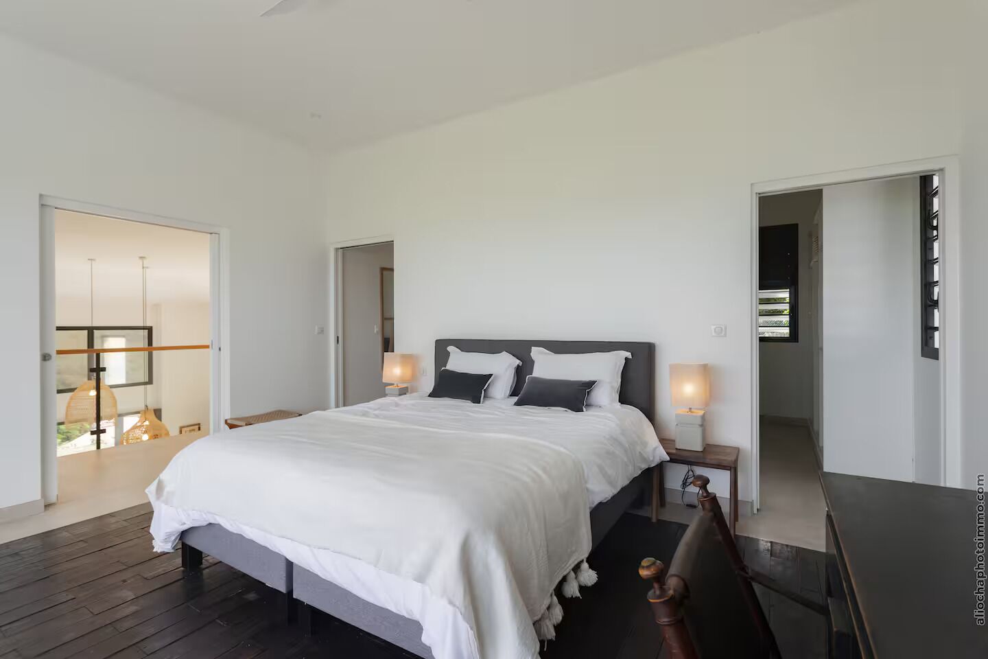 A modern bedroom with a large bed, bedside lamps, and a view of a balcony.