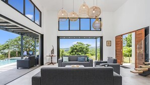Ein modernes Wohnzimmer mit grauem Sofa, einem Couchtisch und Blick auf einen Swimmingpool und Grünflächen.