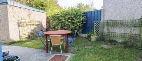 A patio area with a round table and chairs, surrounded by a garden and a blue fence.