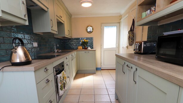 A kitchen with light-colored cabinets, a kettle, a microwave, and a sink. - 11 Penygroes (Holyhead)