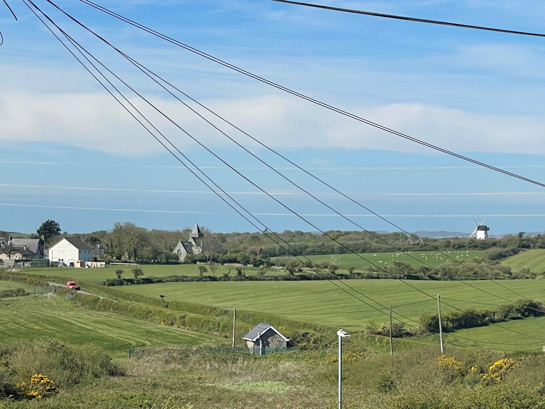 A rural landscape with fields, a windmill, and a few buildings.