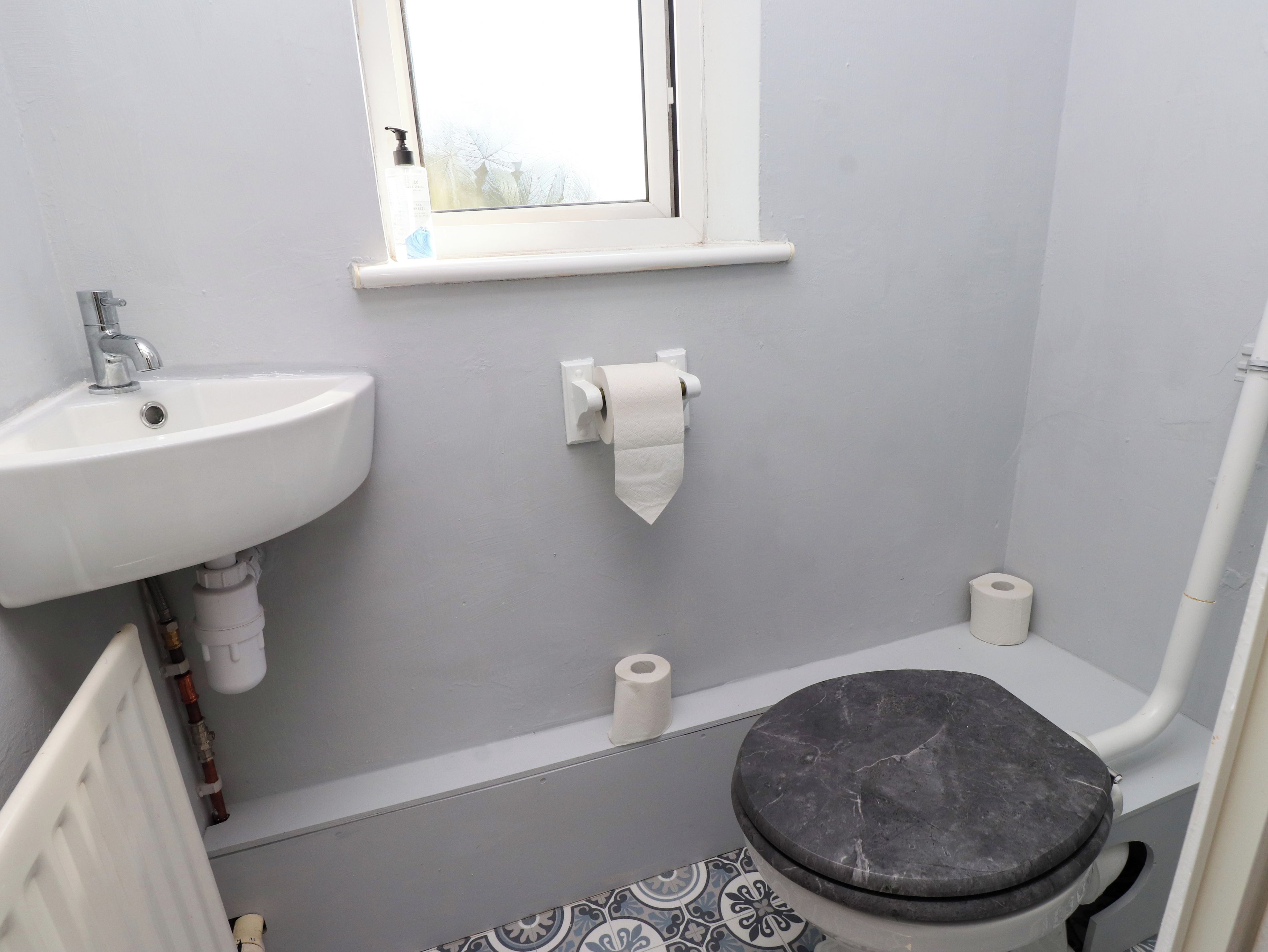 Un bagno con lavandino bianco, water e una finestra sopra il water.