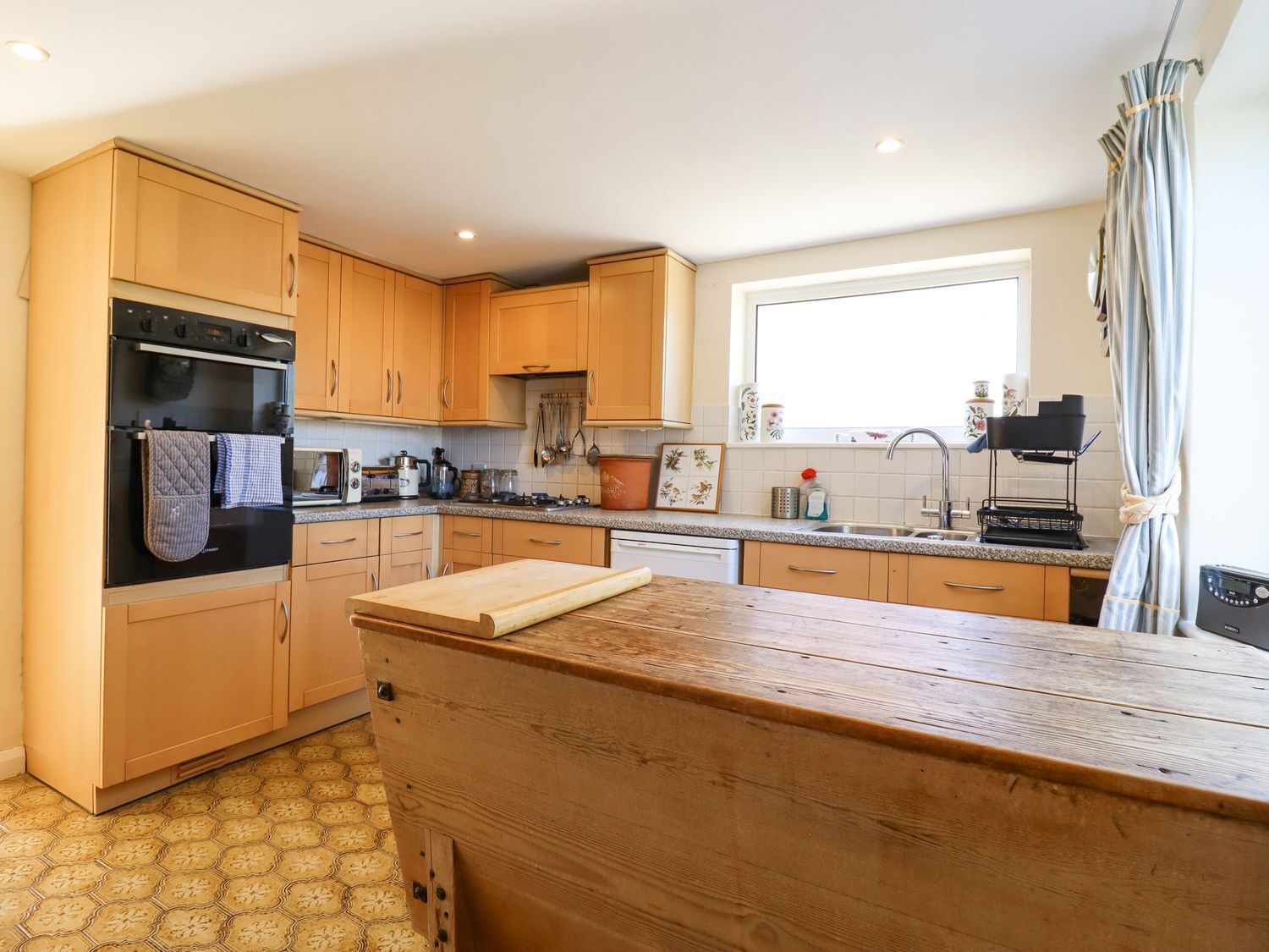 A kitchen with wooden cabinets, a countertop, an oven, a sink, and a window.