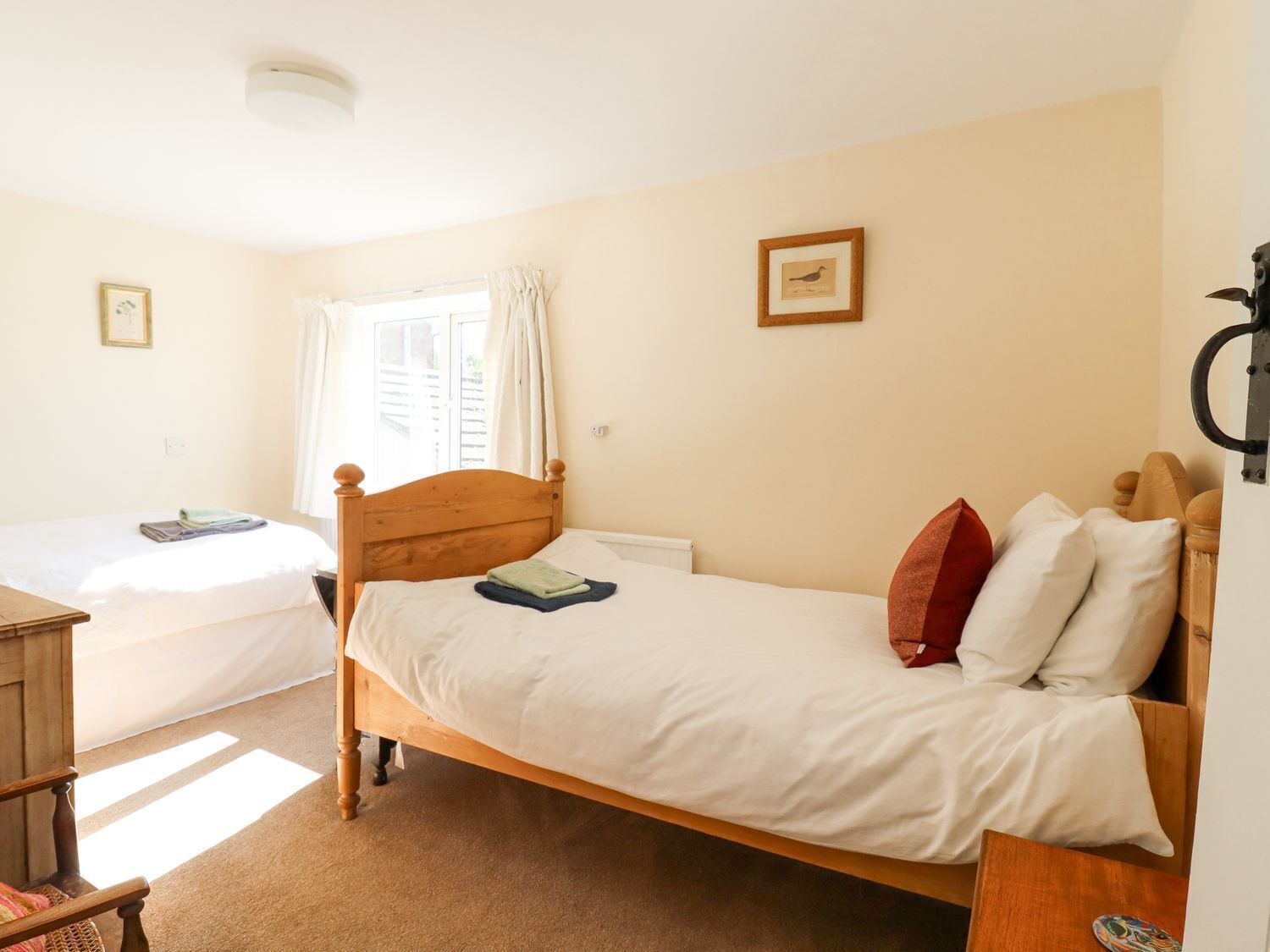 A bedroom with a single bed, a wooden headboard, a window with curtains, and a small bedside table.