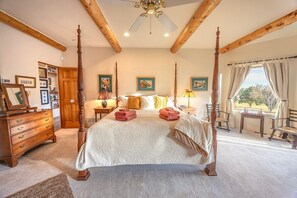 Ein Schlafzimmer mit Himmelbett, Holzbalken, Deckenventilator und Blick ins Freie.