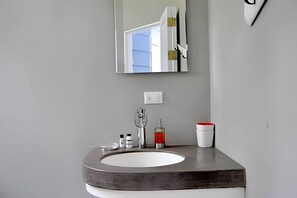 A bathroom with a white sink, a mirror, and a red soap dispenser.