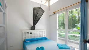 Un dormitorio con cama, mosquitero y vista a la vegetación por la ventana.