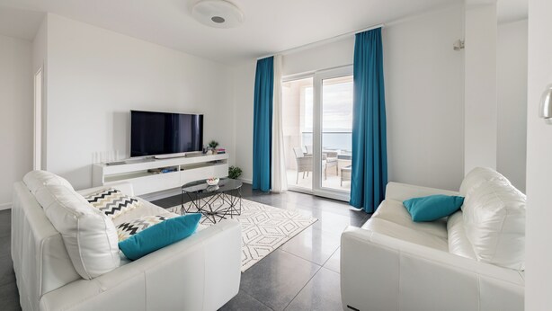 Een moderne woonkamer met een witte bank, een flatscreen televisie en een eethoek met een tafel en stoelen.