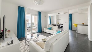 Een moderne woonkamer met een witte bank, een klein bijzettafeltje en een televisie. Er is een schuifdeur naar een balkon.