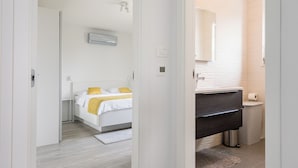 Hotelkamer met een bed, een badkamer met wastafel en spiegel, en een gang met een deur die naar een andere kamer leidt.
