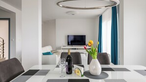 Een moderne eethoek met een witte tafel, zwart-grijze placemats, een wijnfles en een vaas met bloemen.