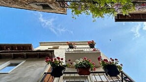 Un bâtiment à la façade en pierre, un balcon orné de plantes en pot et un ciel dégagé.