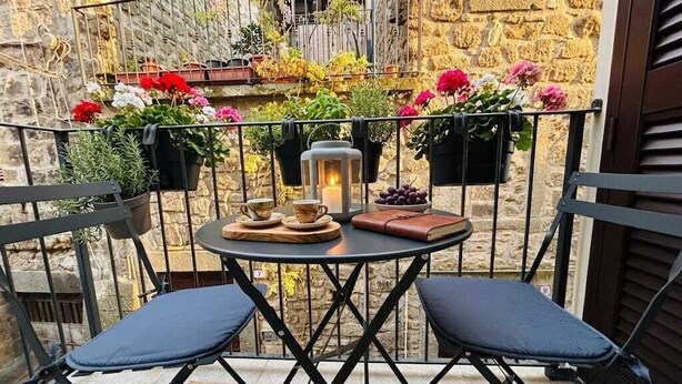 Un balcon avec une table ronde, deux chaises, une lanterne et des plantes en pot.