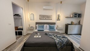 Une chambre moderne comprenant un lit, des tables de chevet, un climatiseur, une armoire et un petit coin cuisine.