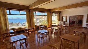 A spacious room with wooden tables and chairs, large windows with curtains, and a fireplace. - Del Lago Sky Hotel (San Carlos de Bariloche)