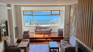 A spacious living room with a large window offering a view of the sea, a fireplace, and a cozy seating area. - Del Lago Sky Hotel (San Carlos de Bariloche)