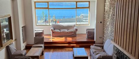 Un salón espacioso con un ventanal que ofrece vistas al mar, una chimenea y una zona de estar acogedora.