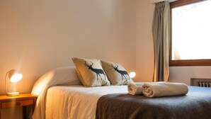 A neatly made bed with two pillows featuring deer silhouettes, a folded towel, and a bedside lamp on a wooden nightstand. - Del Lago Sky Hotel (San Carlos de Bariloche)