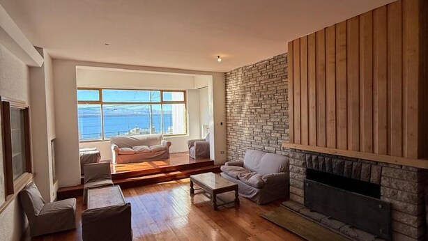 A spacious living room with a stone fireplace, wooden flooring, and a large window offering a view of the sea. - Del Lago Sky Hotel (San Carlos de Bariloche)