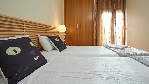 A bedroom with two beds, wooden headboard, a wardrobe, and a nightstand with a lamp.