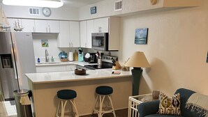 A modern kitchen with white cabinets, a central island, and a dining area with a green sofa and a coffee table. - 1 bedroom on Okaloosa Island FtWalton1 minute walk to the beach. Clean,spacious. (Fort Walton Beach)
