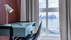 A modern office space with a desk, chair, and lamp. A large window offers a view of a city skyline and water. - The Sands by Wynwood House (Panama City)