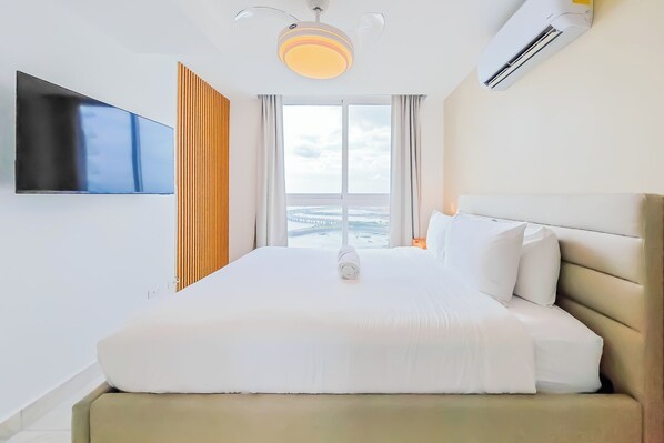 Habitación de hotel con cama, televisión, ventilador de techo y ventana con vista.