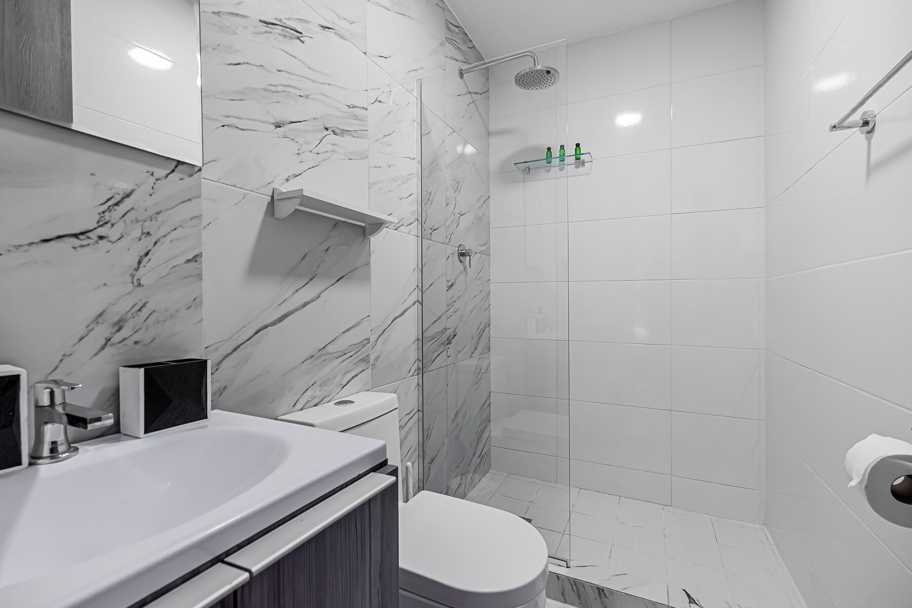 A modern bathroom with a marble backsplash, a white sink, a toilet, and a glass shower enclosure.