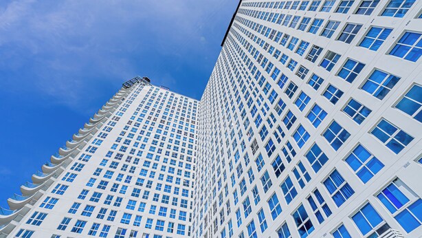 A tall, modern building with a grid of windows and a clear blue sky in the background.