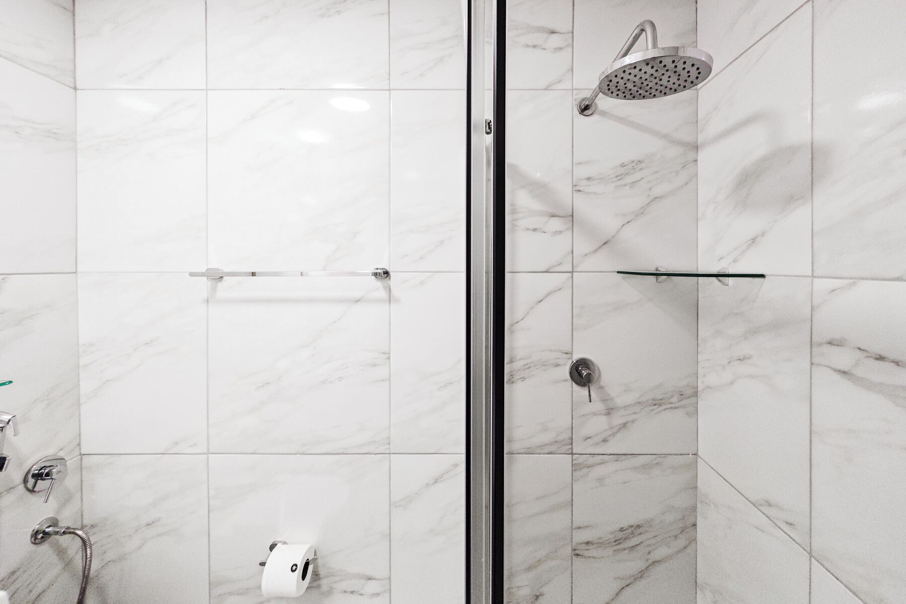 A modern bathroom with a glass shower enclosure, a handheld showerhead, and a toilet paper holder.
