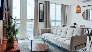 A modern living room with a sofa, a glass coffee table, a dining table with chairs, and large windows offering a city view. - The Sands by Wynwood House (Panama City)